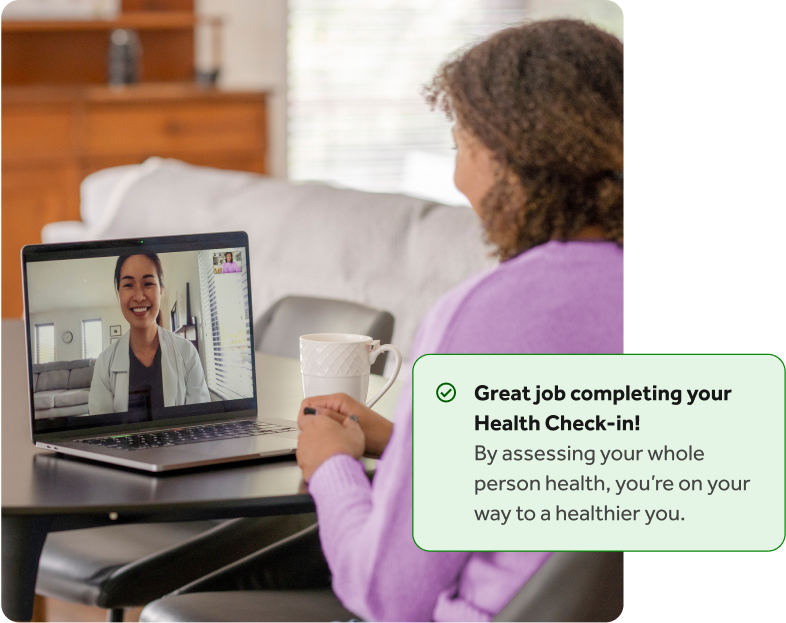 Woman with curly hair in a purple shirt talking to a doctor on her laptop at a table, with an overlay of a Teladoc Health health check-in completion notification.