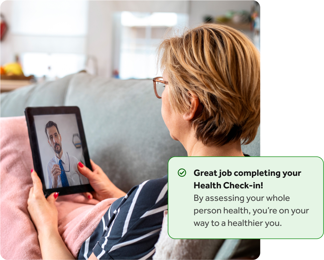 Woman sitting on a couch with her tablet having a video call with a doctor, with an overlay of a Teladoc Health health check-in completion notification.