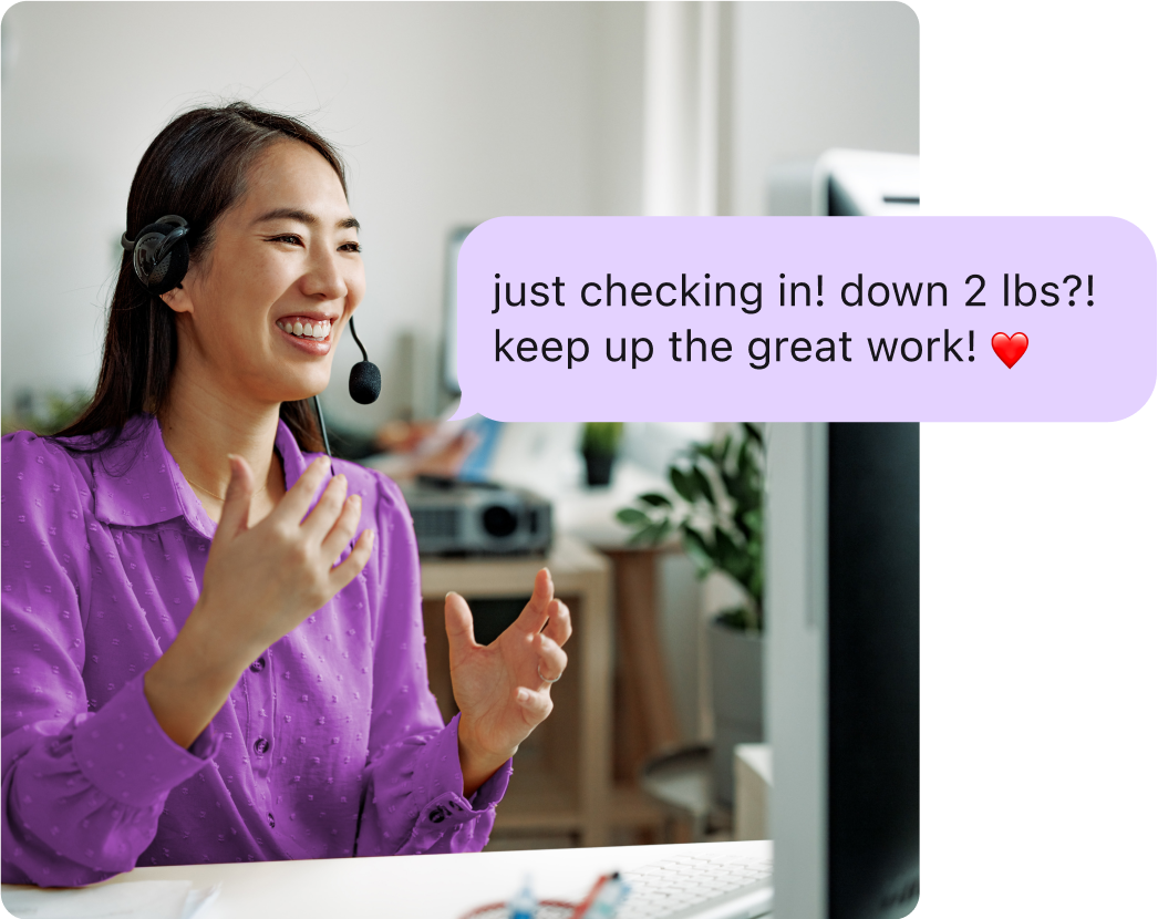 Woman with a headset smiling and talking to her computer, with an overlay of a coaching message reading 'Just checking in! Down 2 lbs?! Keep up the great work!'
