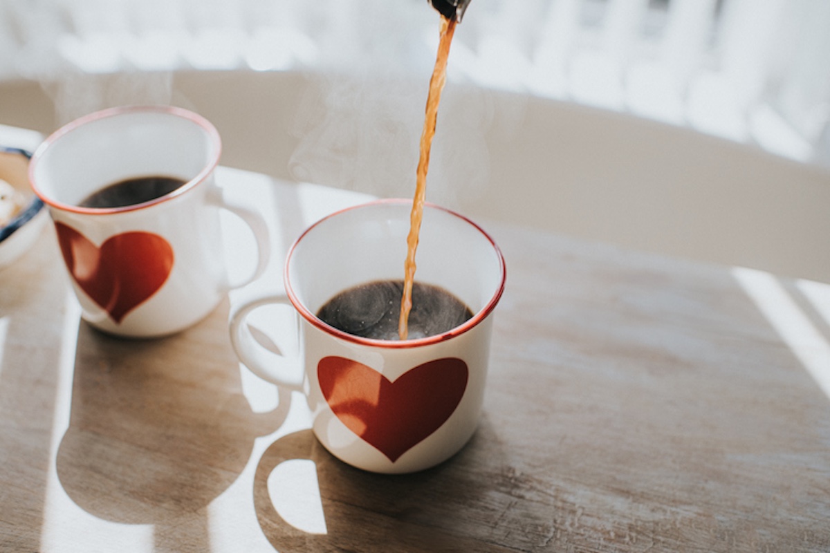 Pouring black coffee into coffee cups with heart design. Space for copy. Conceptual.