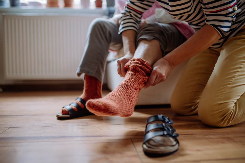 Out of frame senior woman getting help from caregiver with putting on socks.
