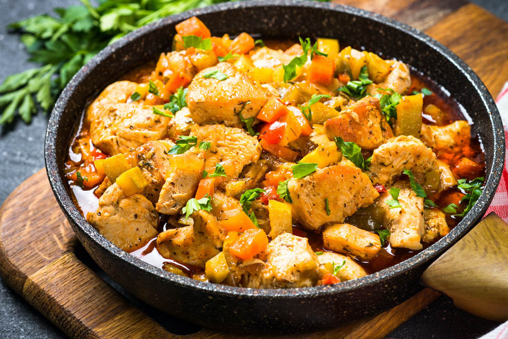 Sartén con trozos de pollo guisados y verduras frescas, decorado con perejil.