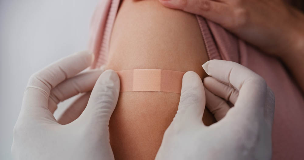 Manos con guantes aplicando una venda en la parte superior del brazo de una persona