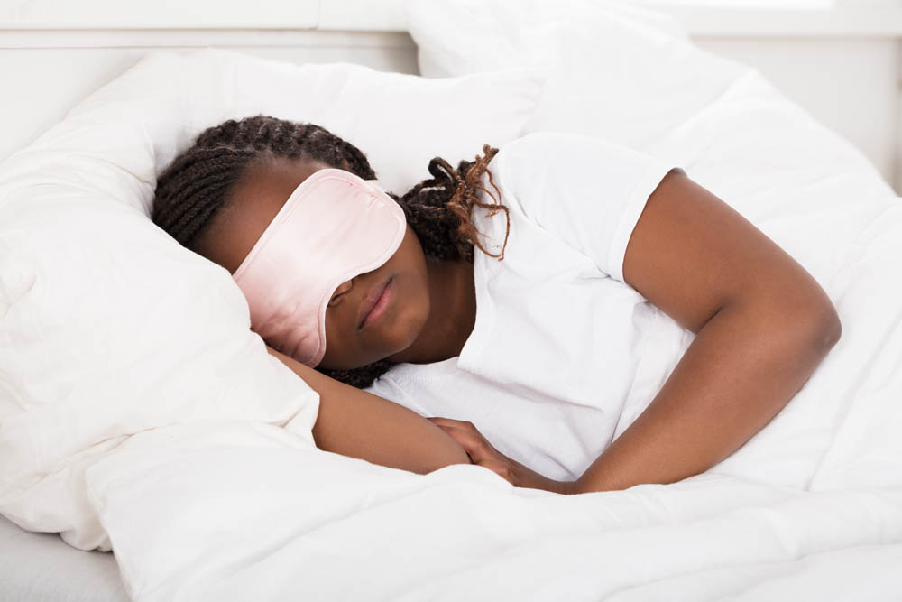 Primer plano de una niña africana con antifaz rosa durmiendo en la cama