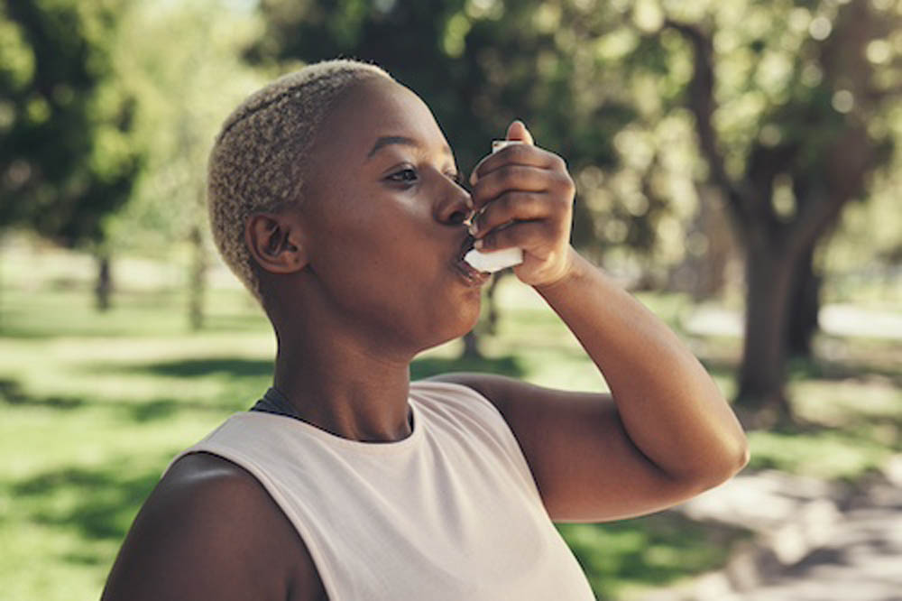 Mujer usando un inhalador al aire libre en un parque.