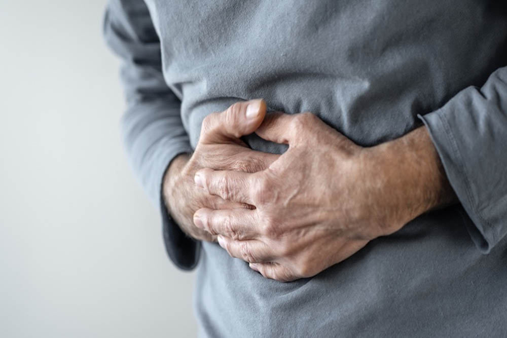 Hombre sujetándose el estómago con molestia, usando un suéter gris.